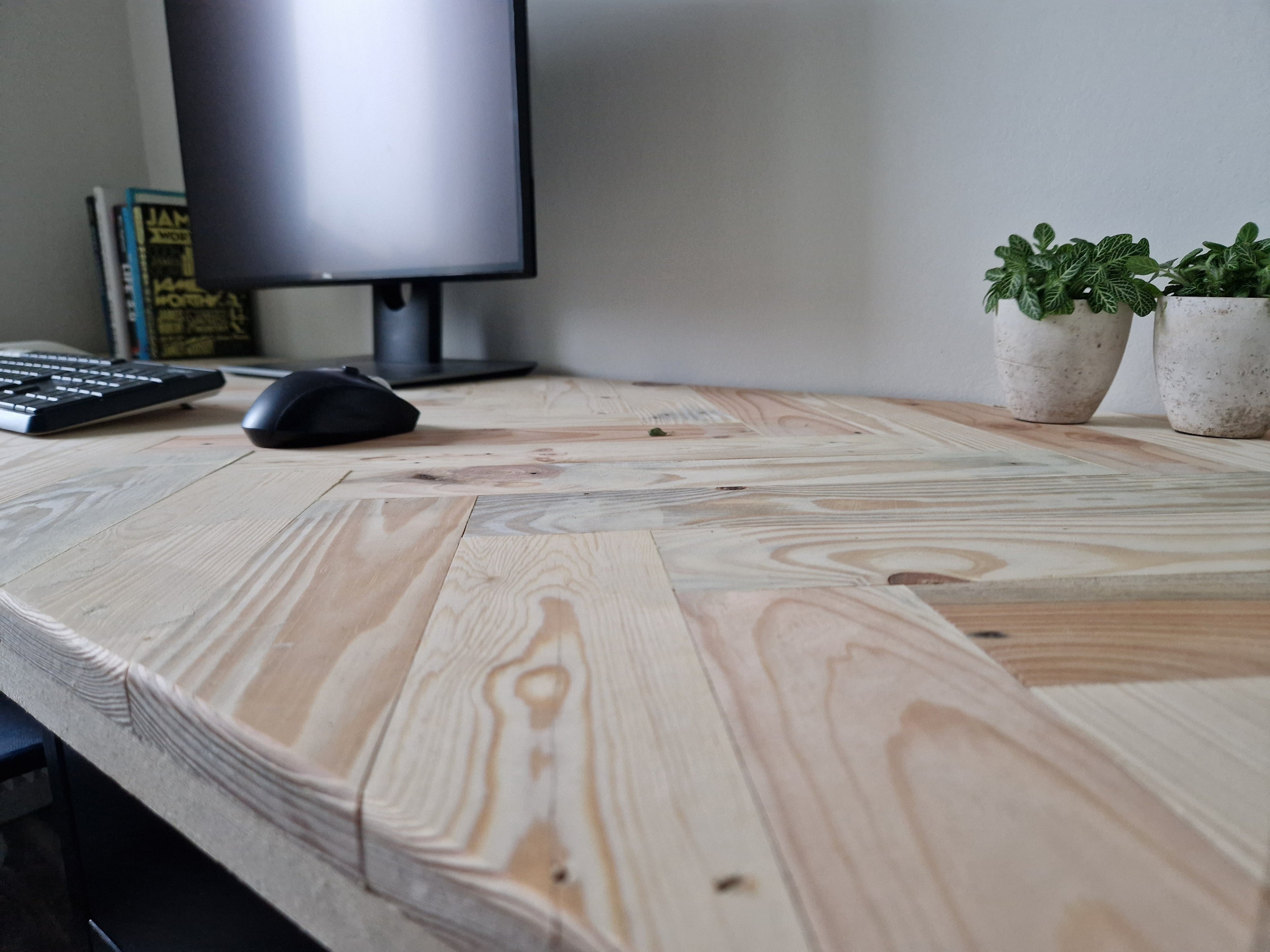 Houten bureaublad met visgraat patroon van recycled hout met een monitor, muis, toetsenbord en planten in pot.